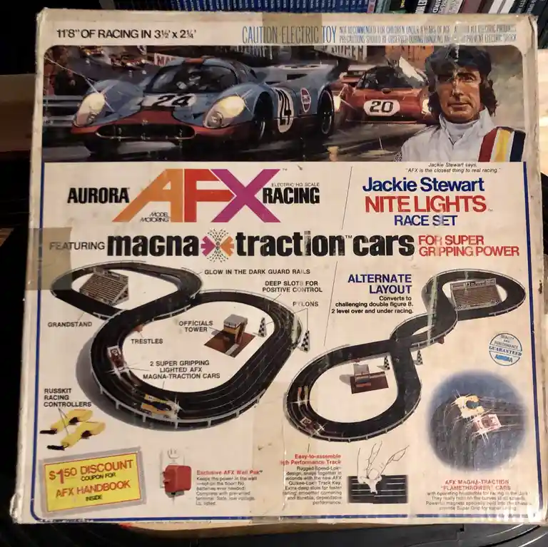 The image shows a vintage Aurora AFX Racing toy set box featuring Jackie Stewart. The box art depicts racing cars and a…
