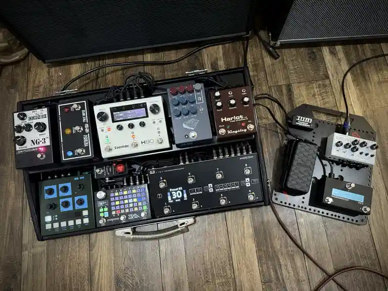 An overhead shot of a musician's extensive pedalboard setup on a wooden floor, featuring numerous guitar effects pedals like…