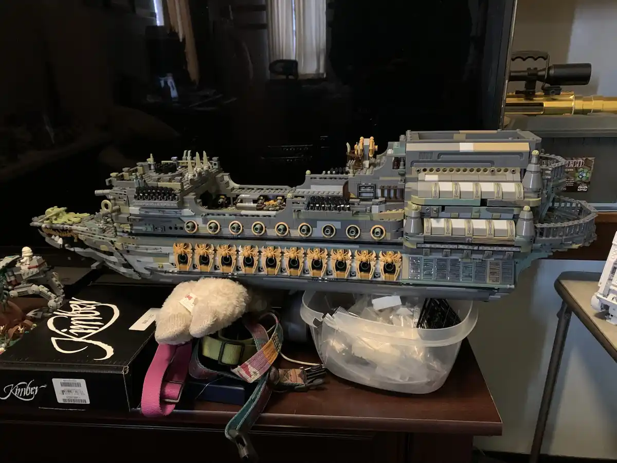 A large, partially assembled LEGO spaceship model rests on a wooden table, with visible internal components and missing…