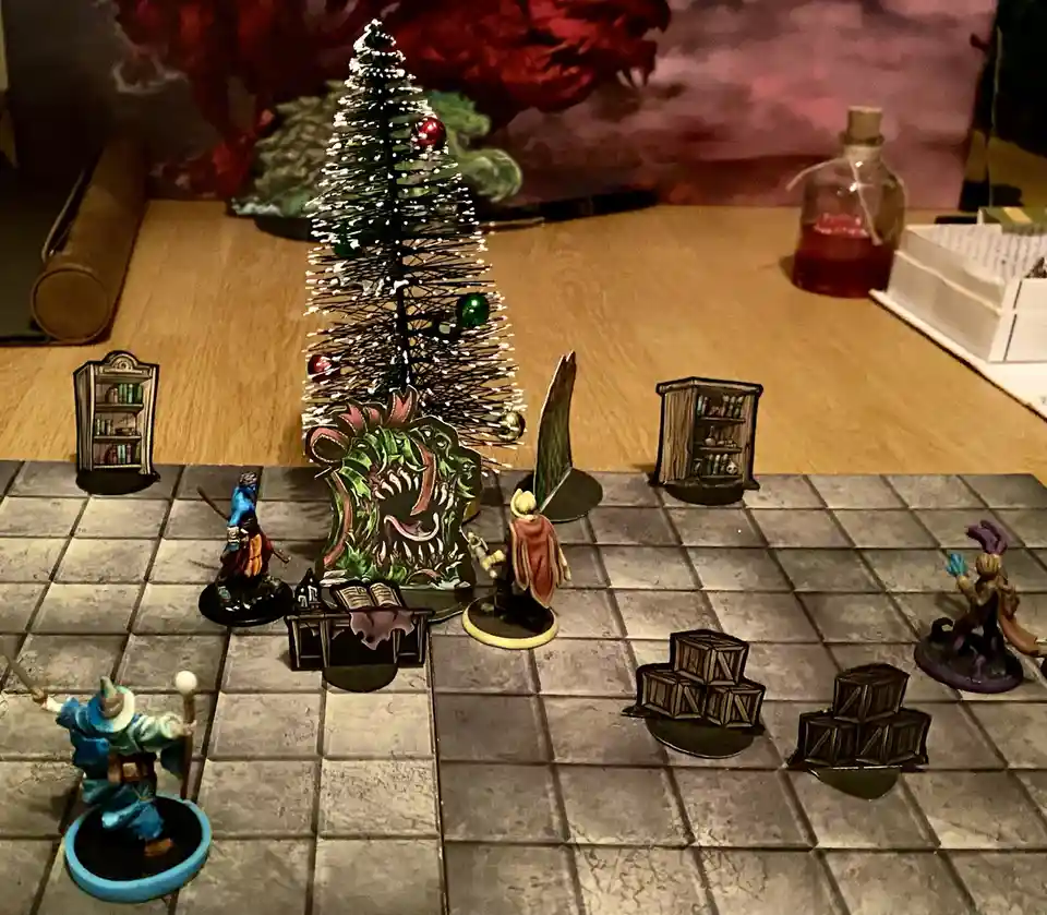 A tabletop role-playing game scene features miniature figures on a tiled floor, with a small, decorated Christmas tree…