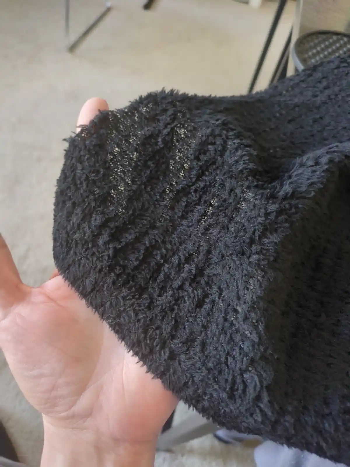 A hand holds up a black, fuzzy, textured fabric that appears to be a sweater sleeve, but the overlaid text humorously claims…