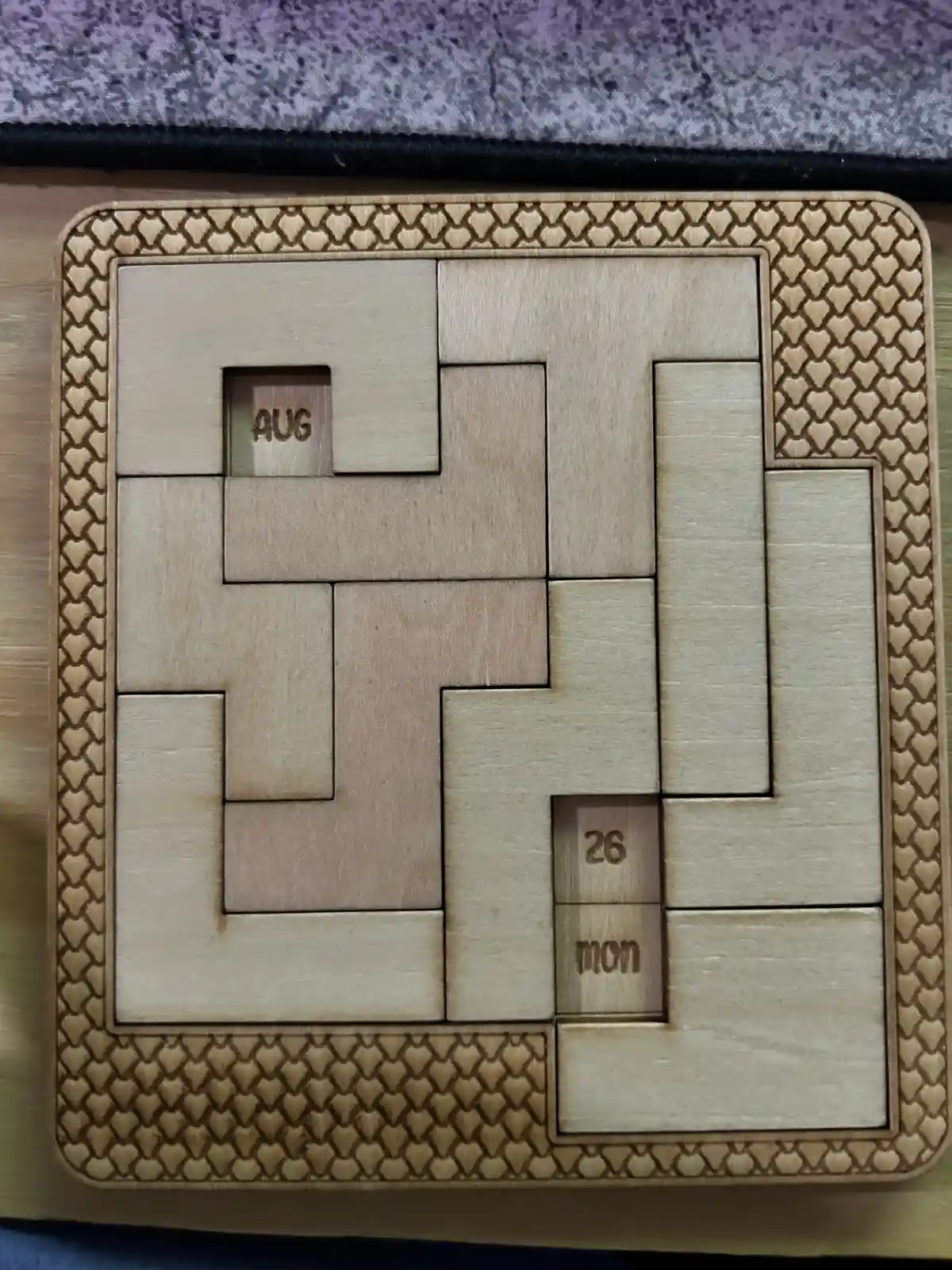 A wooden puzzle calendar with interlocking pieces forming a grid, where two small pieces reveal the text 'aug' and '26 mon'…