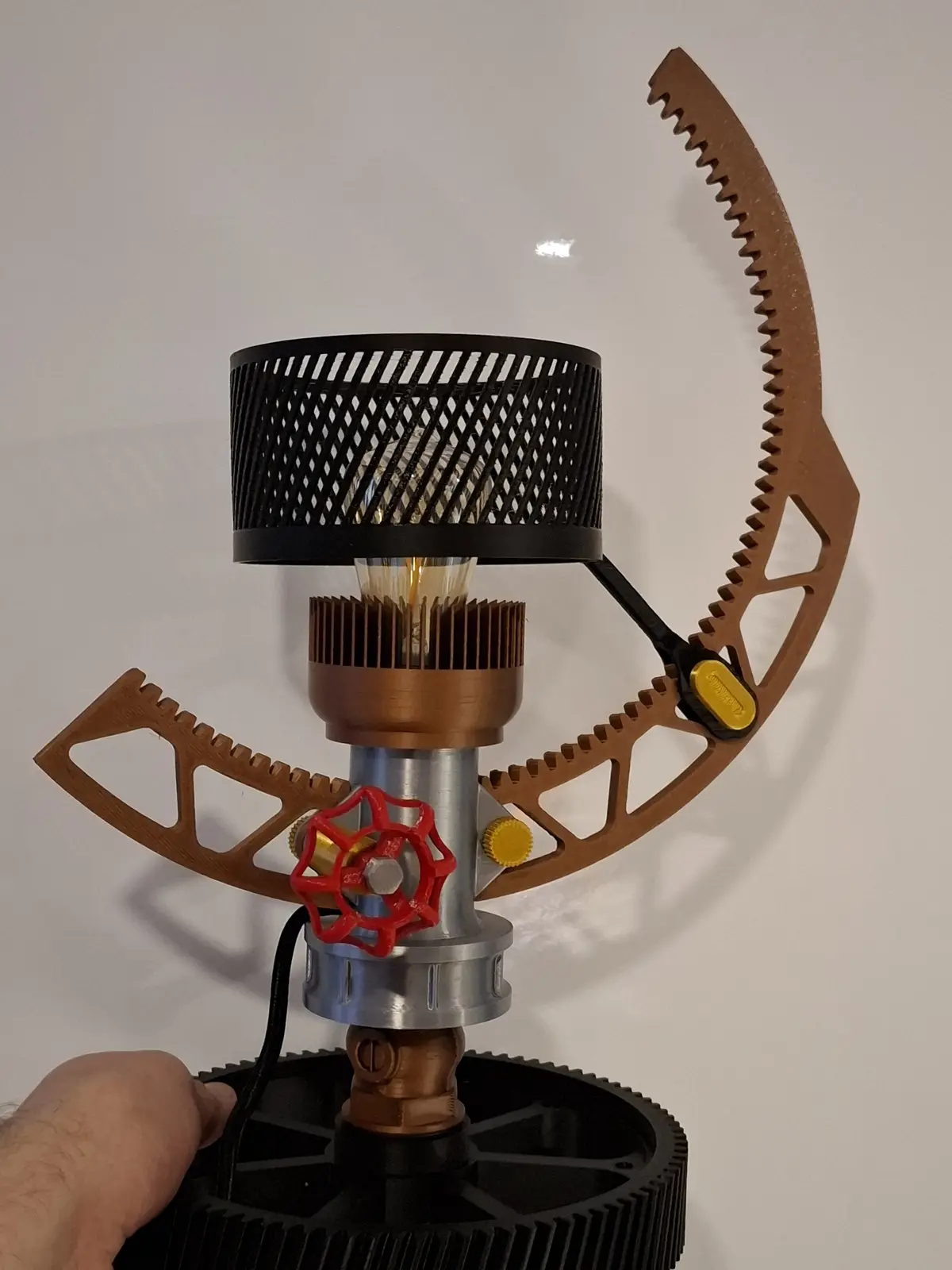 A lamp with a black mesh shade and an exposed Edison bulb is constructed from industrial-looking metal parts, including…