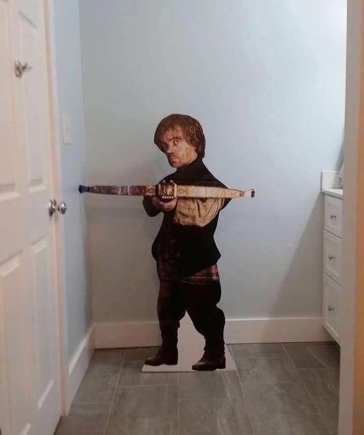 A life-sized cardboard cutout of Tyrion Lannister from Game of Thrones stands in a hallway, holding a sword horizontally…