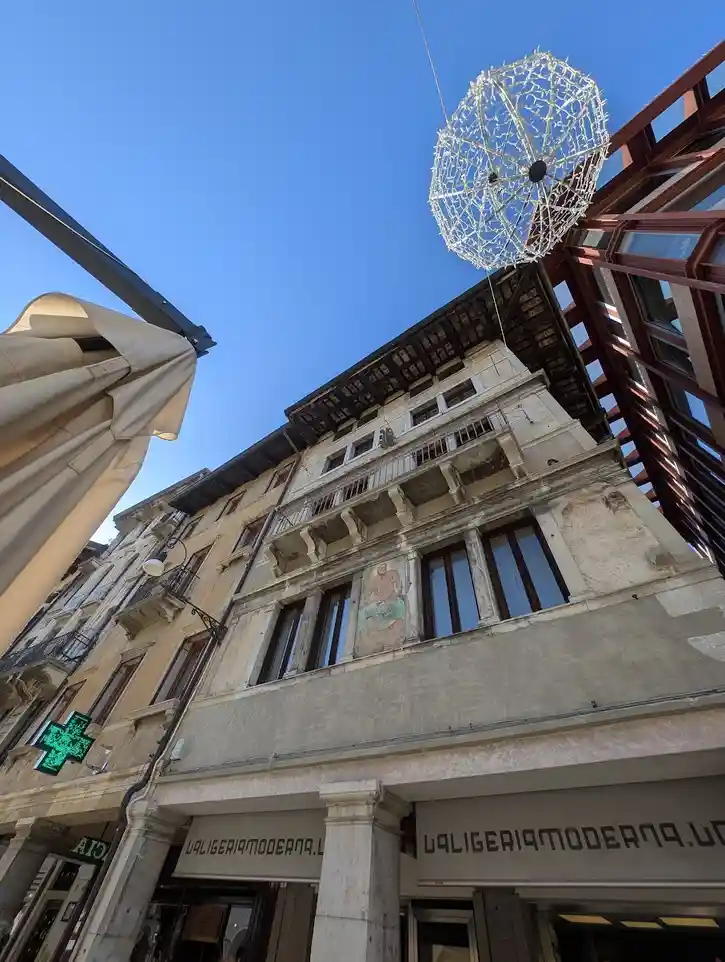 A low-angle photo shows a large, white, wireframe umbrella-like structure hanging from above against a clear blue sky…