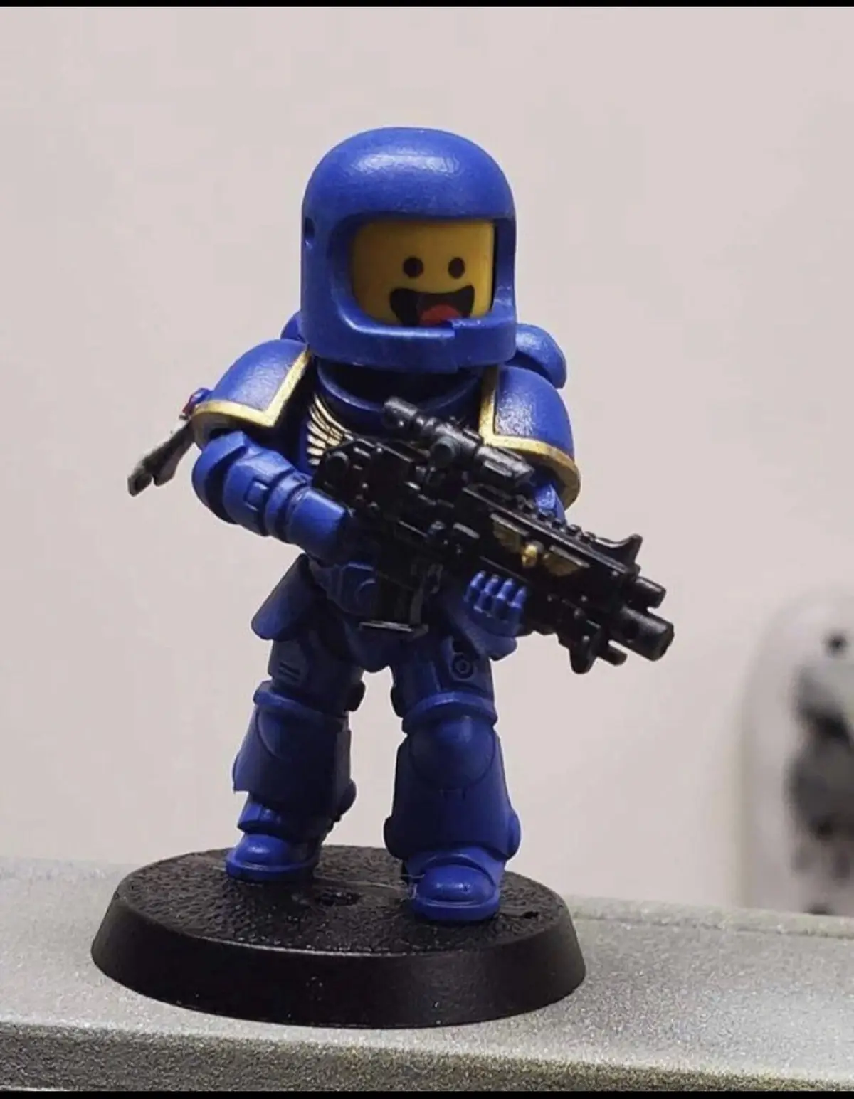 A custom-painted Lego minifigure dressed in blue Warhammer 40k Space Marine armor, holding a detailed black bolter rifle…