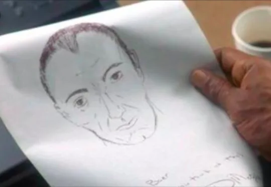 A hand holds a sketch of a man's face, drawn in pencil, with a coffee cup visible in the background. The sketch has…