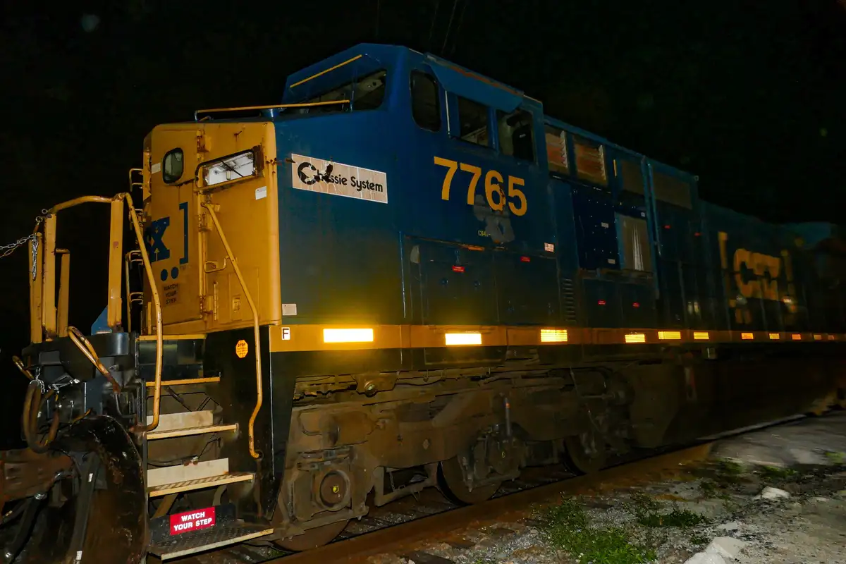 A blue and yellow locomotive, number 7765, is shown at night with its headlights on, featuring a 'Chassis System' logo. The…