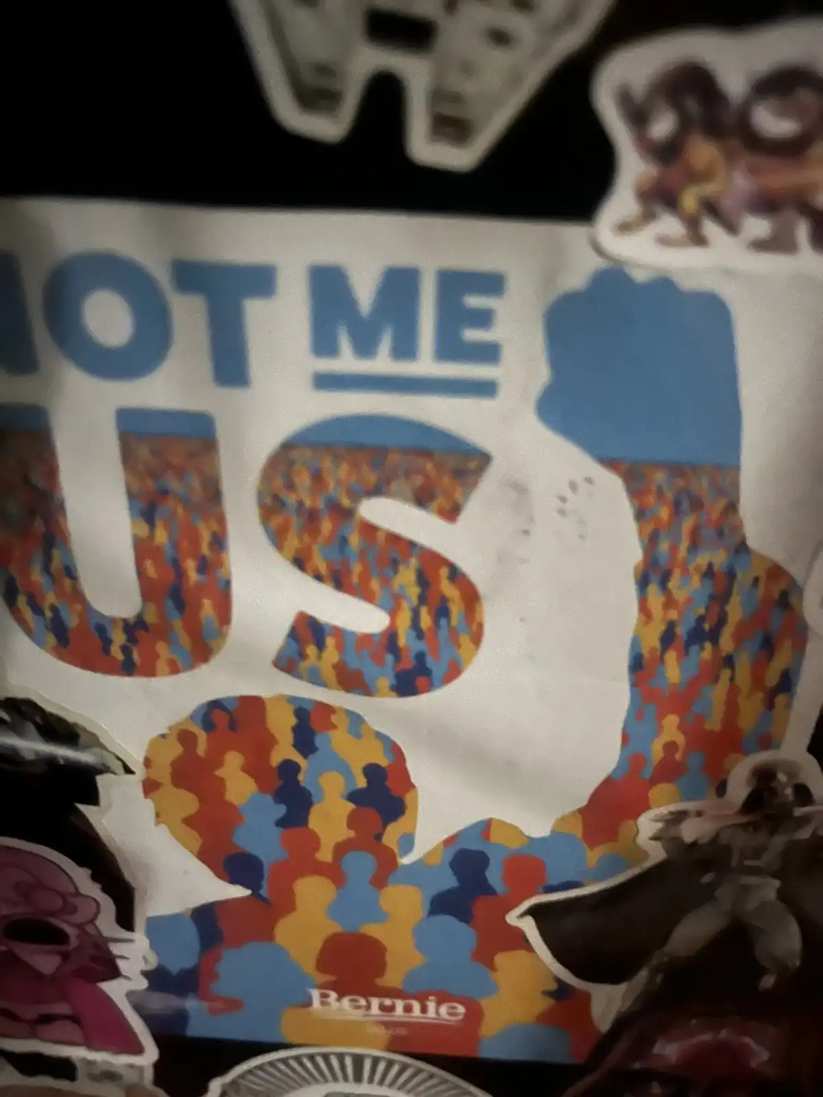 A close-up of a Bernie Sanders 2020 campaign poster showing the text 'NOT ME US' with the word 'US' filled with colorful…