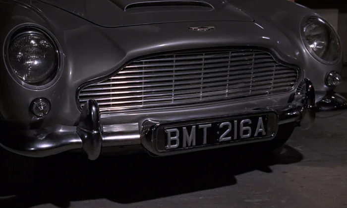The image displays a sequence of six panels showing the front of a silver Aston Martin DB5. The top row shows the license…