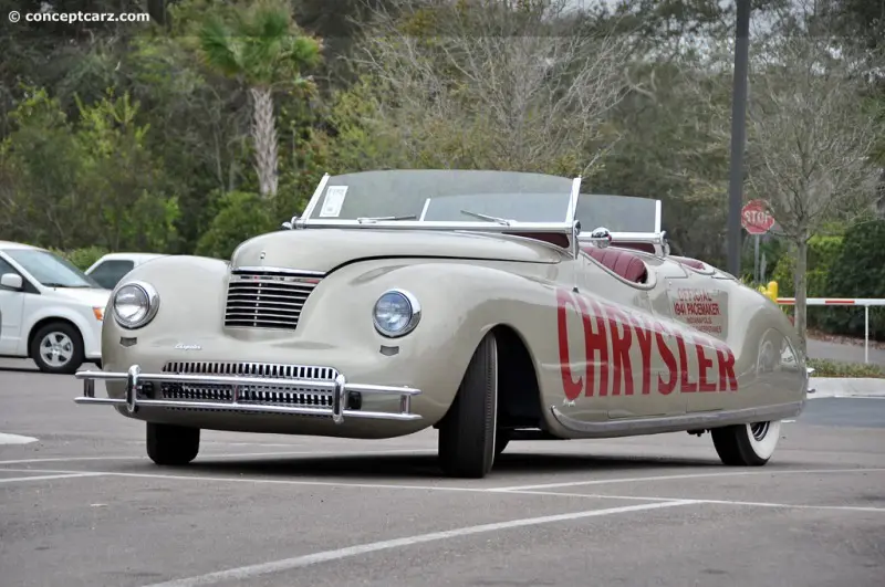 A vintage beige Chrysler convertible with 'CHRYSLER' in large red letters along its side is parked in a lot. The car has a…