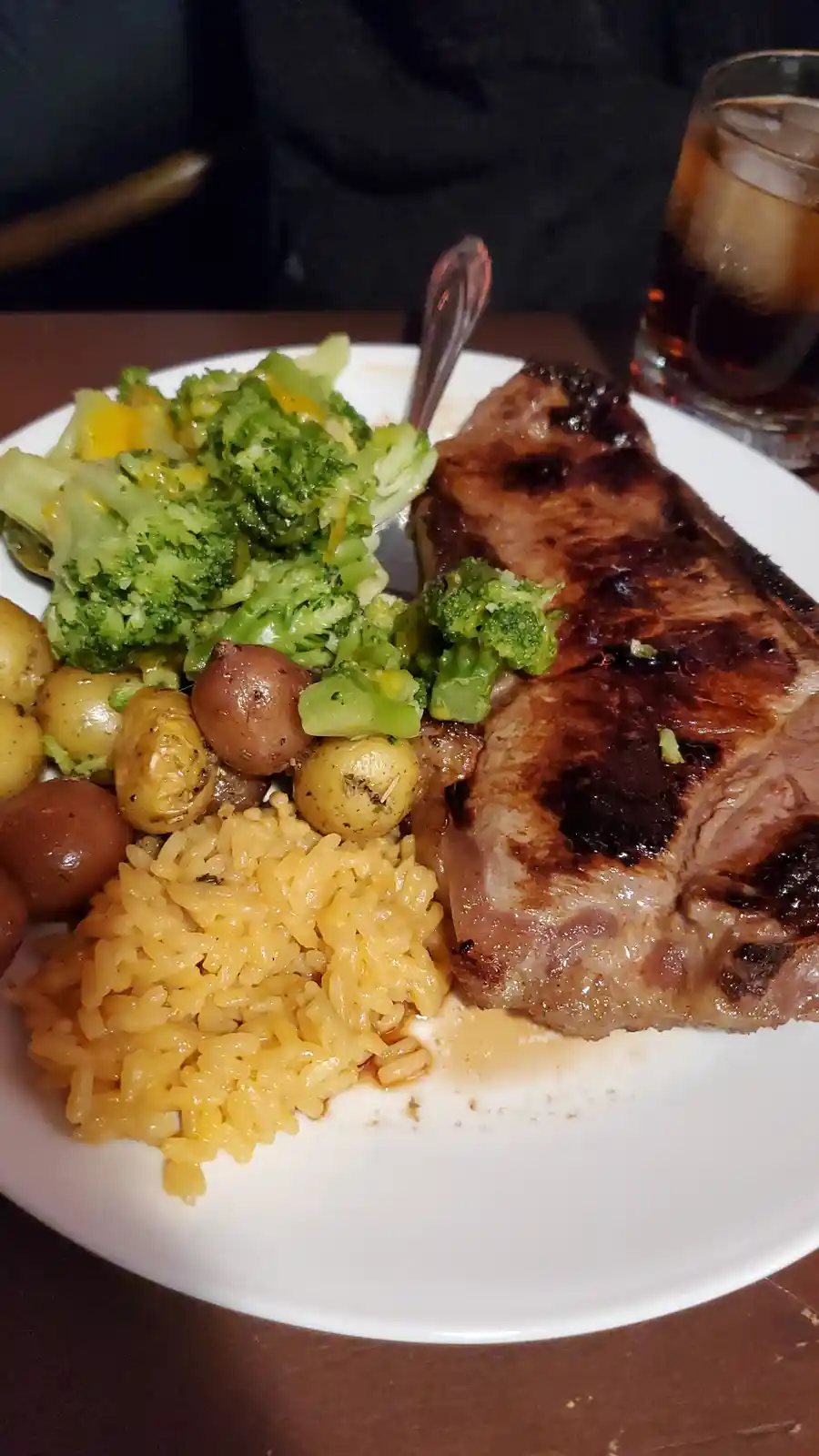 A close-up photo of a plated meal featuring a large grilled steak, a serving of broccoli with cheese sauce, roasted baby…