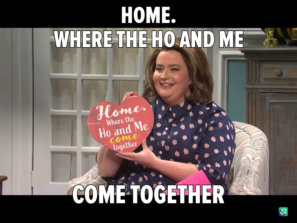 A woman sits in a chair holding a red heart-shaped sign that reads 'Home. Where the Ho and Me come together.' Large white…