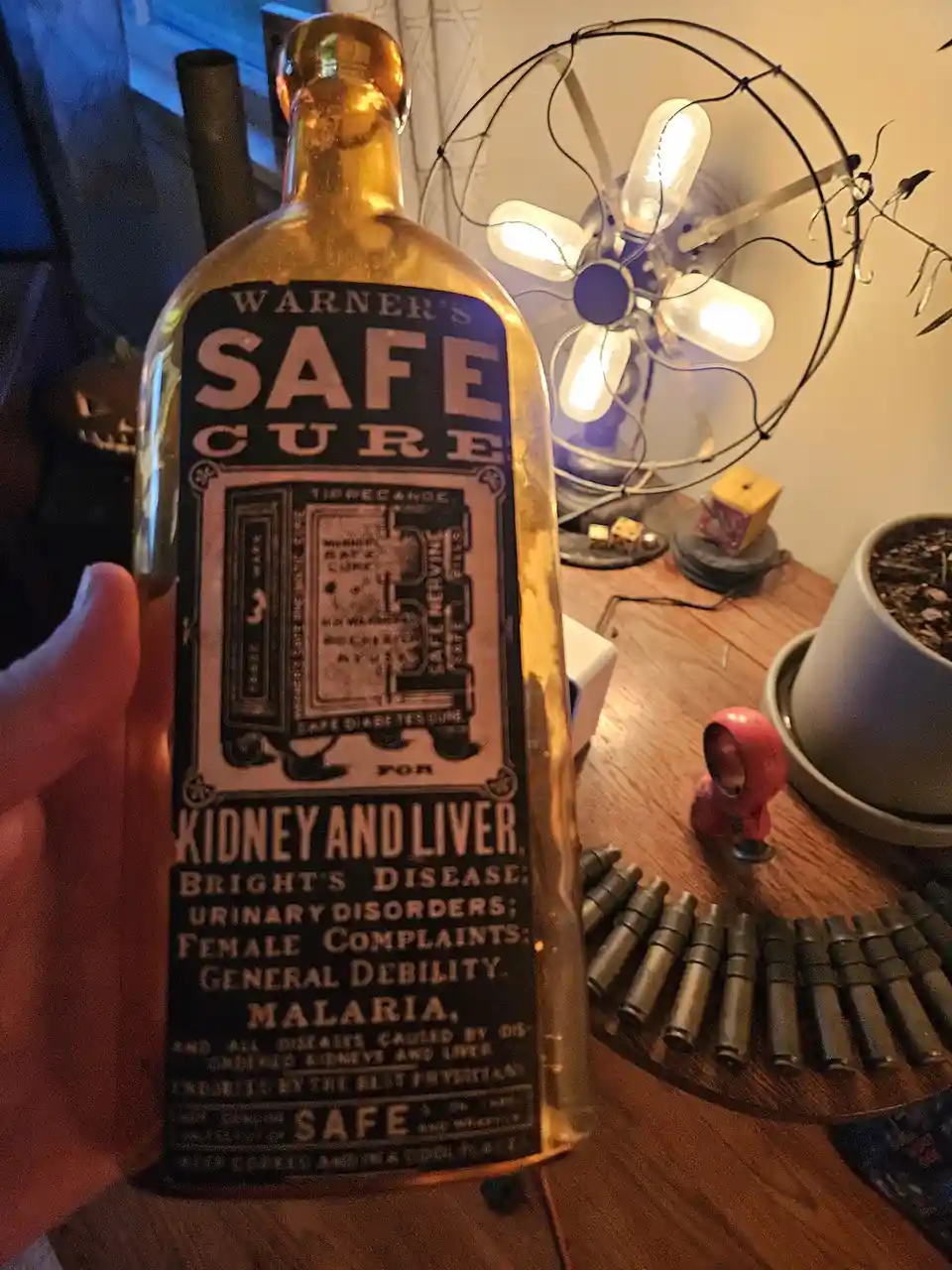 A hand holds a vintage amber glass bottle labeled 'Warner's Safe Cure' for kidney and liver ailments, with a decorative…
