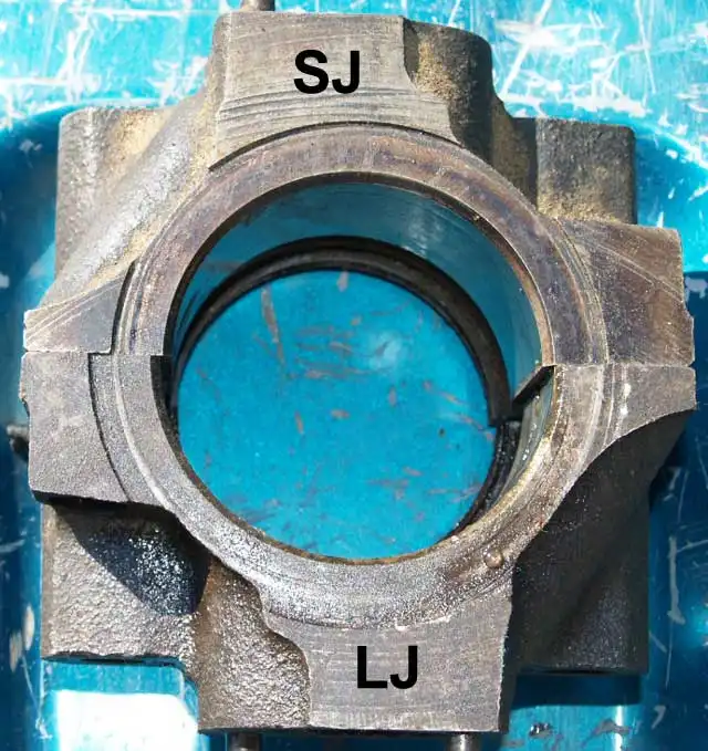 A close-up of a worn, dirty metal mechanical part with a circular opening revealing a bright blue interior. The letters 'SJ'…