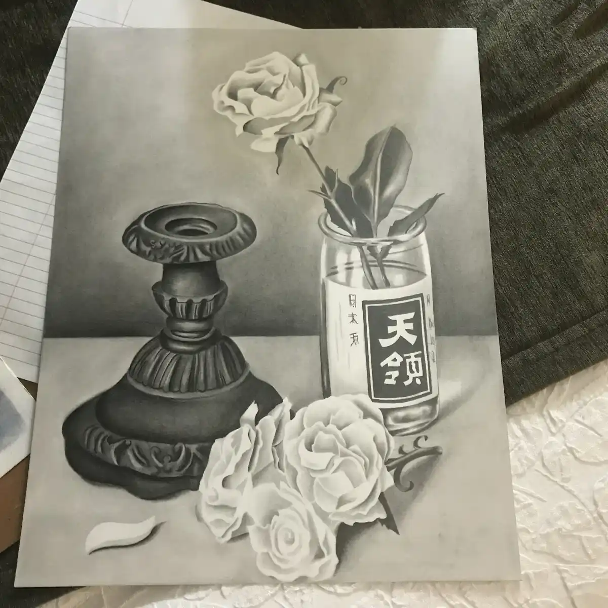 A detailed pencil drawing of a still life featuring a decorative candlestick, a glass bottle labeled with Japanese…