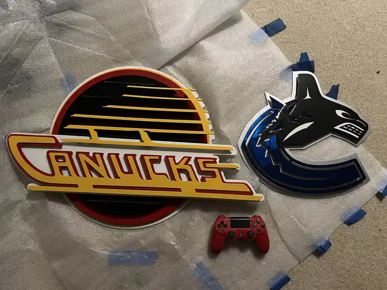Two 3D-printed Vancouver Canucks hockey team logos lie on bubble wrap, one the old retro sunburst design and the other the…