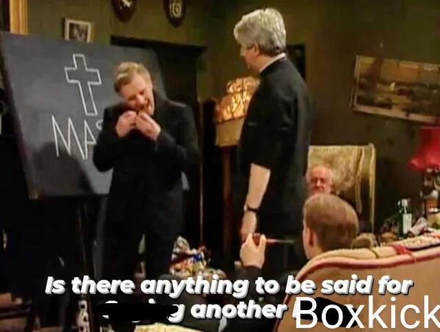 A man in a black suit stands in front of a blackboard with a white cross and 'MAS' written on it, covering his mouth with…