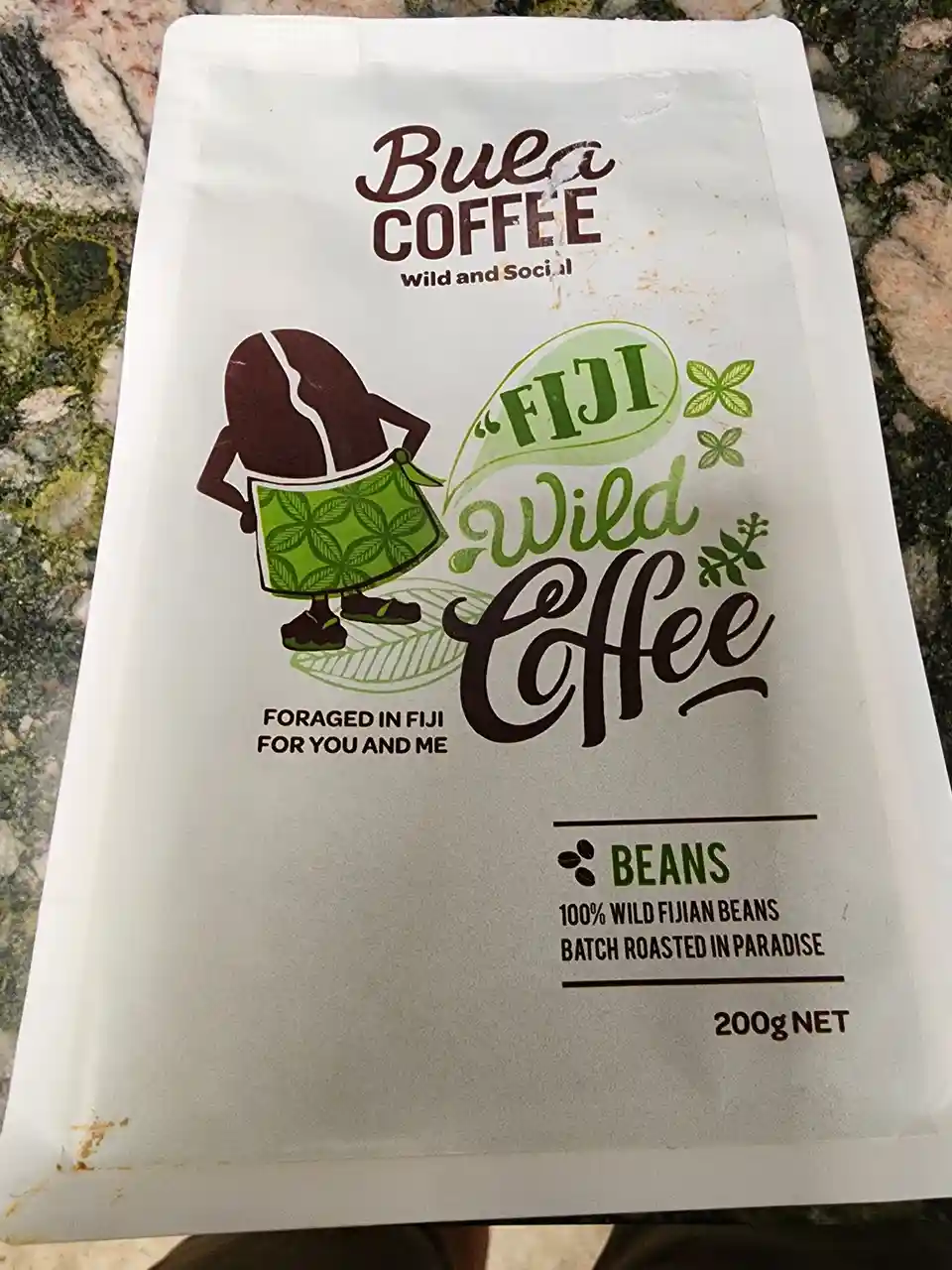 A close-up photo of a white Bula Coffee bag featuring a cartoon coffee bean character wearing a green skirt and standing on…
