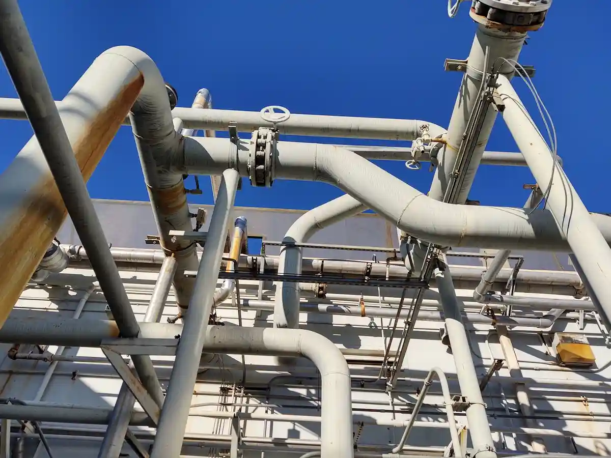 A complex tangle of large, weathered industrial pipes and valves against a clear blue sky, with overlaid text reading 'i'm…