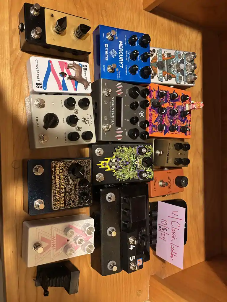 A collection of colorful and uniquely designed guitar effect pedals arranged on a wooden surface, with a handwritten note in…
