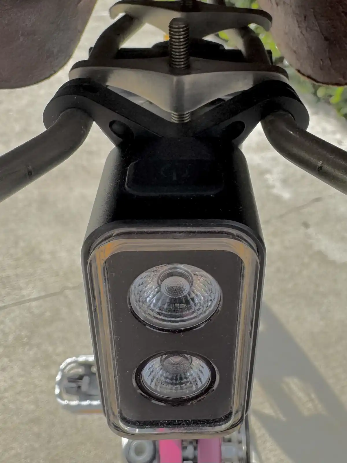 A close-up photo shows a black, rectangular bicycle headlight mounted on handlebars, featuring two circular LED bulbs under…