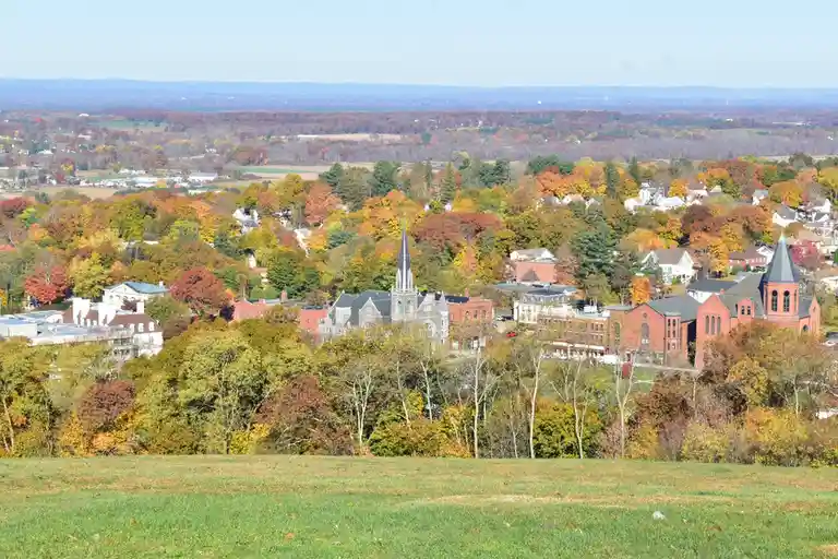 A scenic autumn landscape of a town with colorful trees and historic buildings under a clear sky, overlaid with the text…