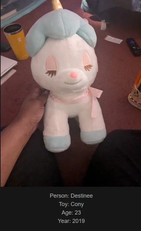 A person holds a white plush unicorn toy with light blue hair and hooves, pink ribbon, and closed eyes. Text overlaid at the…