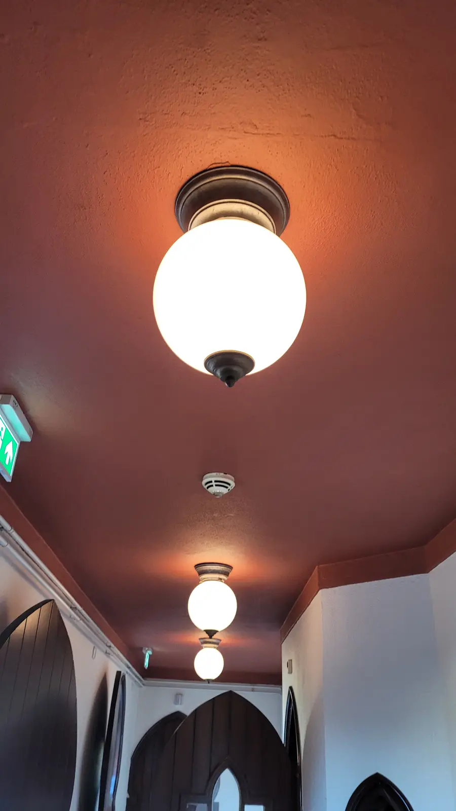 A low-angle shot of a hallway ceiling with a warm-toned, textured reddish-brown surface. A bright, spherical frosted glass…