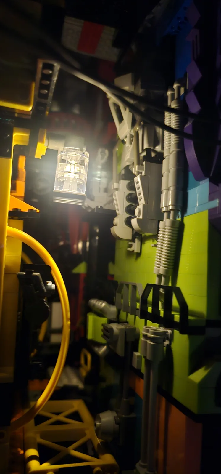 A close-up shot of a complex, dimly lit interior built from colorful Lego bricks, featuring a glowing light fixture, coiled…