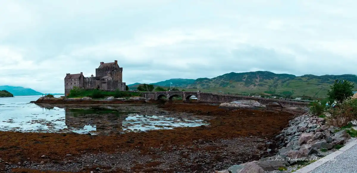 A scenic photograph of Eilean Donan Castle in Scotland, featuring the historic stone castle on an island connected by a…