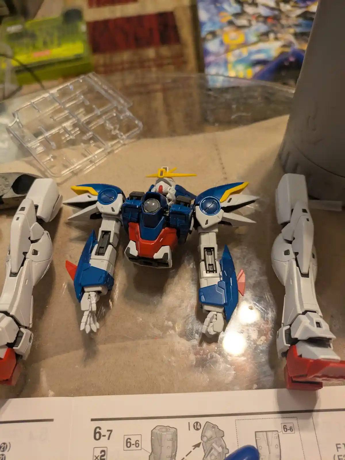 A partially assembled blue, white, and red plastic robot model sits on a work surface, surrounded by its detached limbs and…