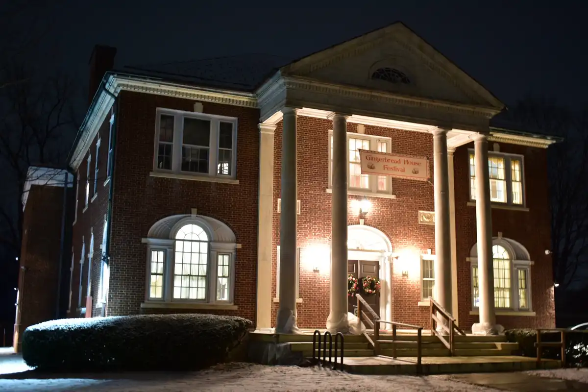 A large, stately brick building with classical columns and arched windows is illuminated at night, with snow on the ground…