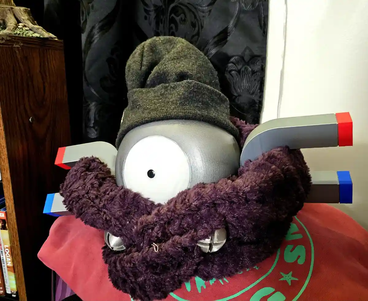 A plush toy resembling a Minion with a gray head, large white eye, and purple fuzzy beard is shown with several large bar…