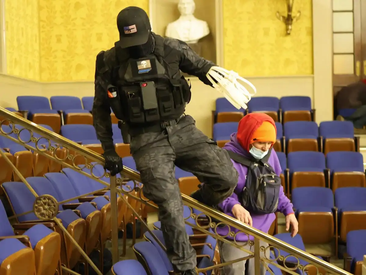 A person in full tactical gear, including a black balaclava, camouflage pants, and a vest with a skull patch, is ascending a…