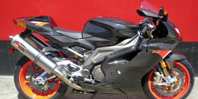 a black and silver sport motorcycle with orange wheels and carbon fiber bodywork is parked against a red wall. the overlaid…