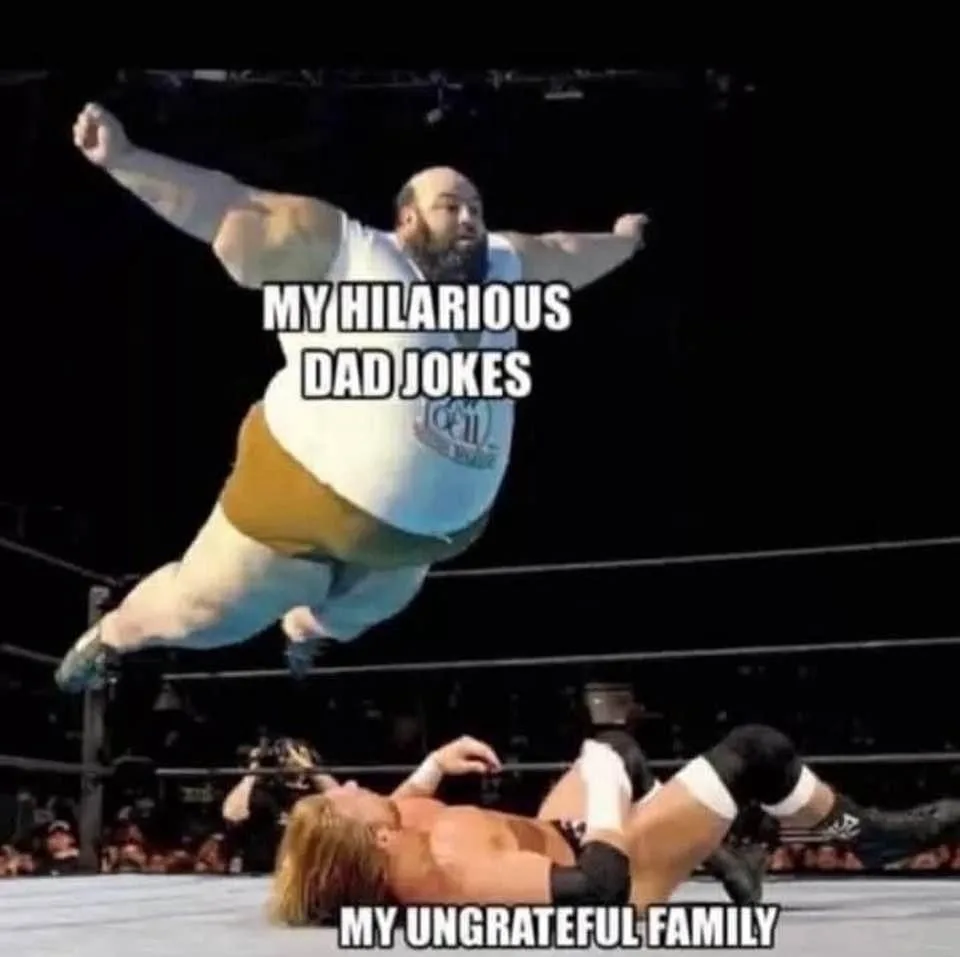 A large, bearded wrestler in a white tank top and tan trunks leaps mid-air toward another wrestler lying prone on the mat…