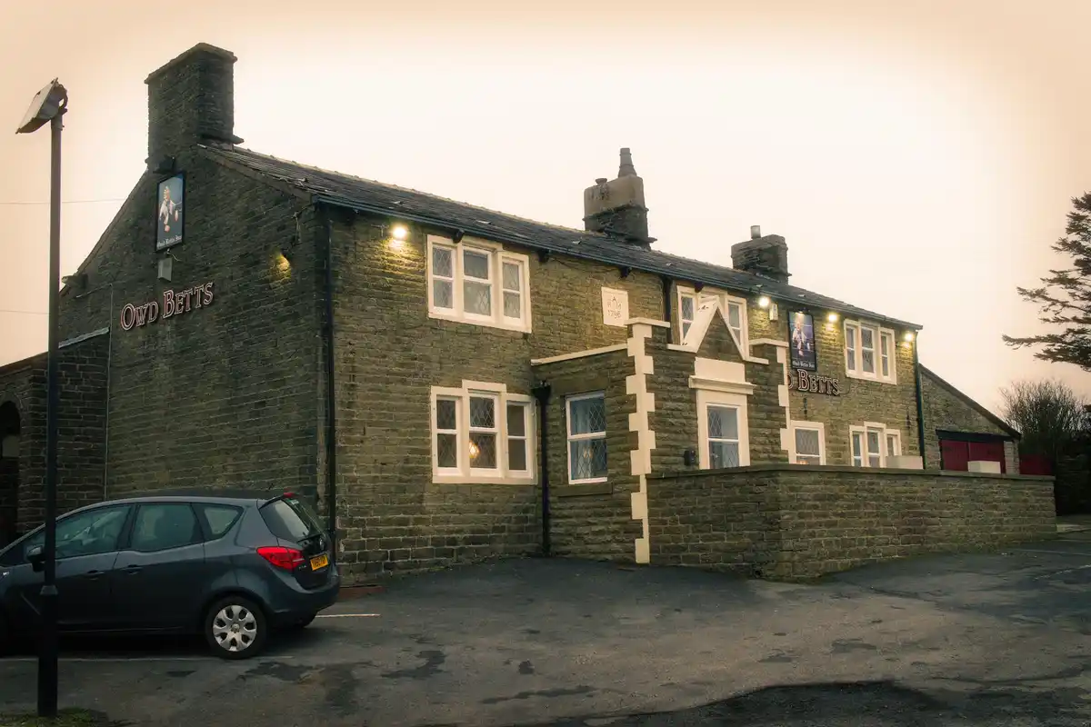 A photo of the Owd Betts pub, a stone building with white-trimmed windows and a sign reading 'Owd Betts' on its facade, with…