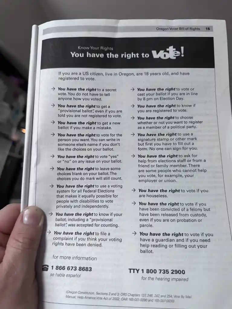 A hand holds open a booklet titled 'Oregon Voter Bill of Rights,' page 15, which lists numerous voter rights in bullet…