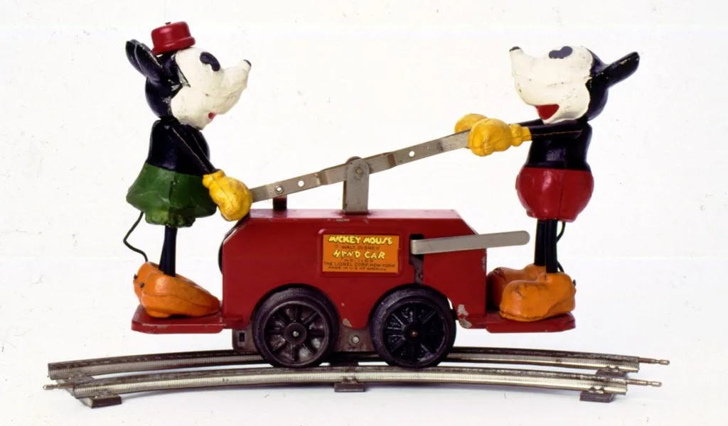 A vintage tin toy train car labeled 'MICKEY MOUSE HEAD CAR' features two classic Mickey Mouse figures—one in green shorts…