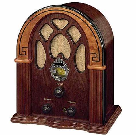 A vintage-style wooden radio with an arched top, decorative cutouts, and knobs labeled 'TUNING', 'AM-FM', and 'VOLUME'. The…