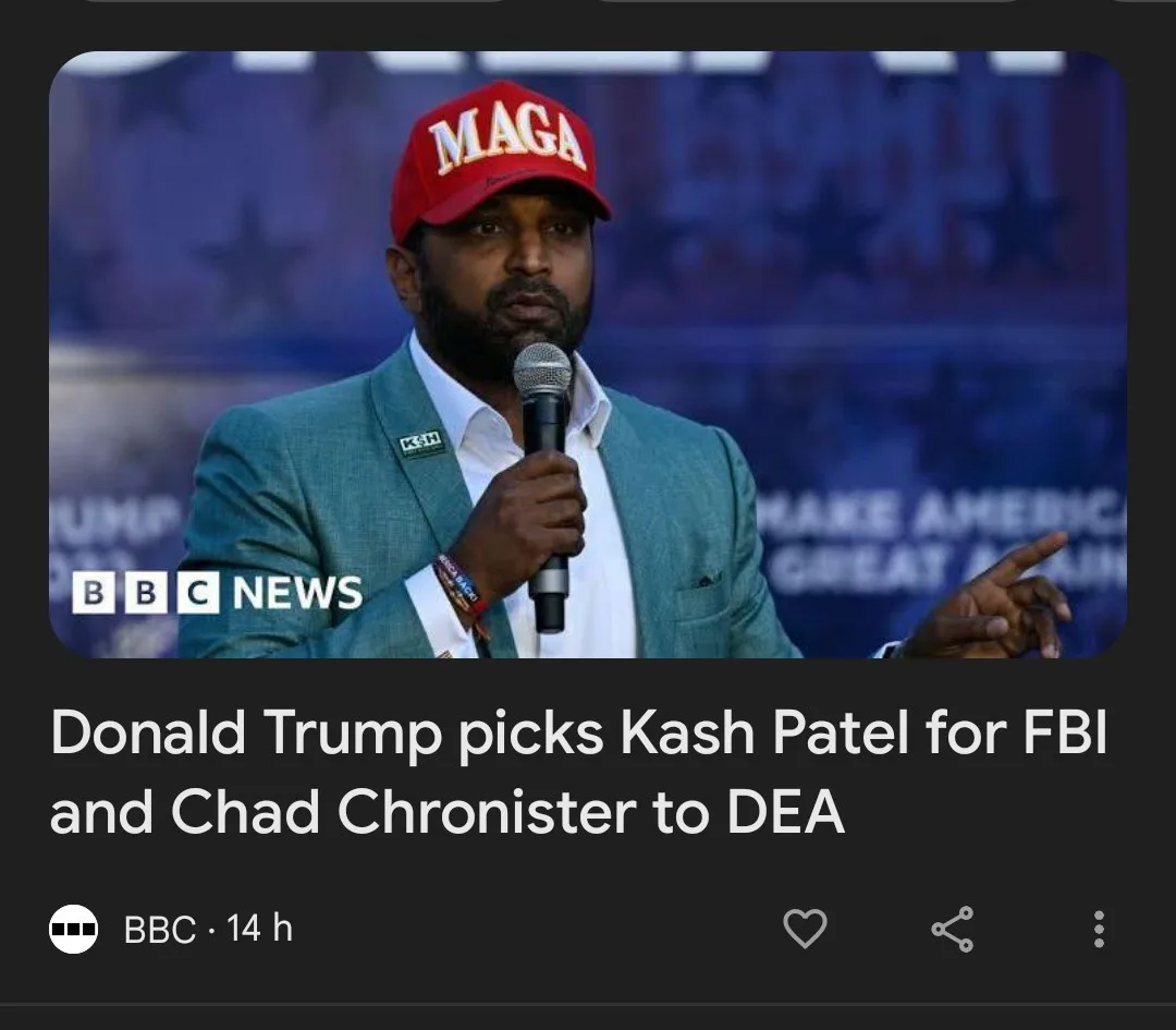 A man with a beard wearing a red MAGA hat and a green suit holds a microphone while speaking, with a blurred background…