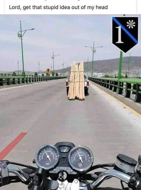 A first-person view from a motorcycle rider looking ahead at a pickup truck driving on a bridge, carrying a tall, precarious…