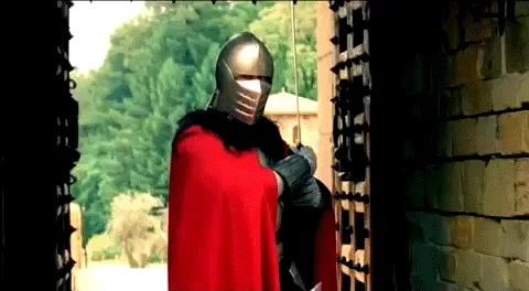 A person in a medieval-style helmet and red cape stands at a castle gate, slowly turning their head to the right in three…