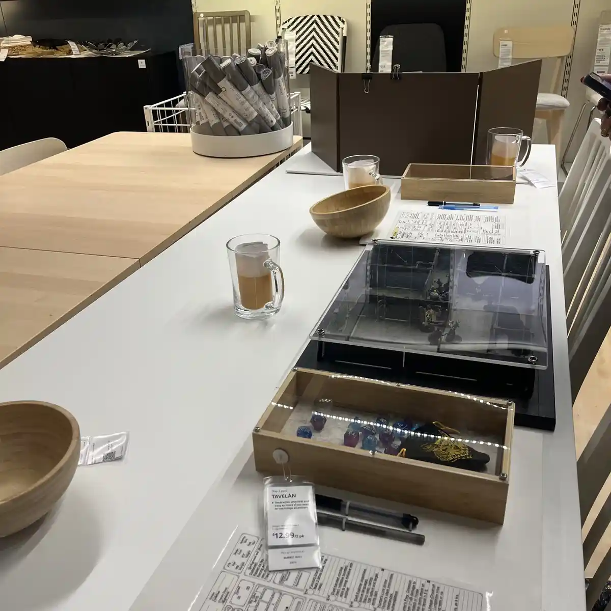 A photo taken inside an IKEA store shows a white display table with various home goods, including wooden bowls, glass mugs…