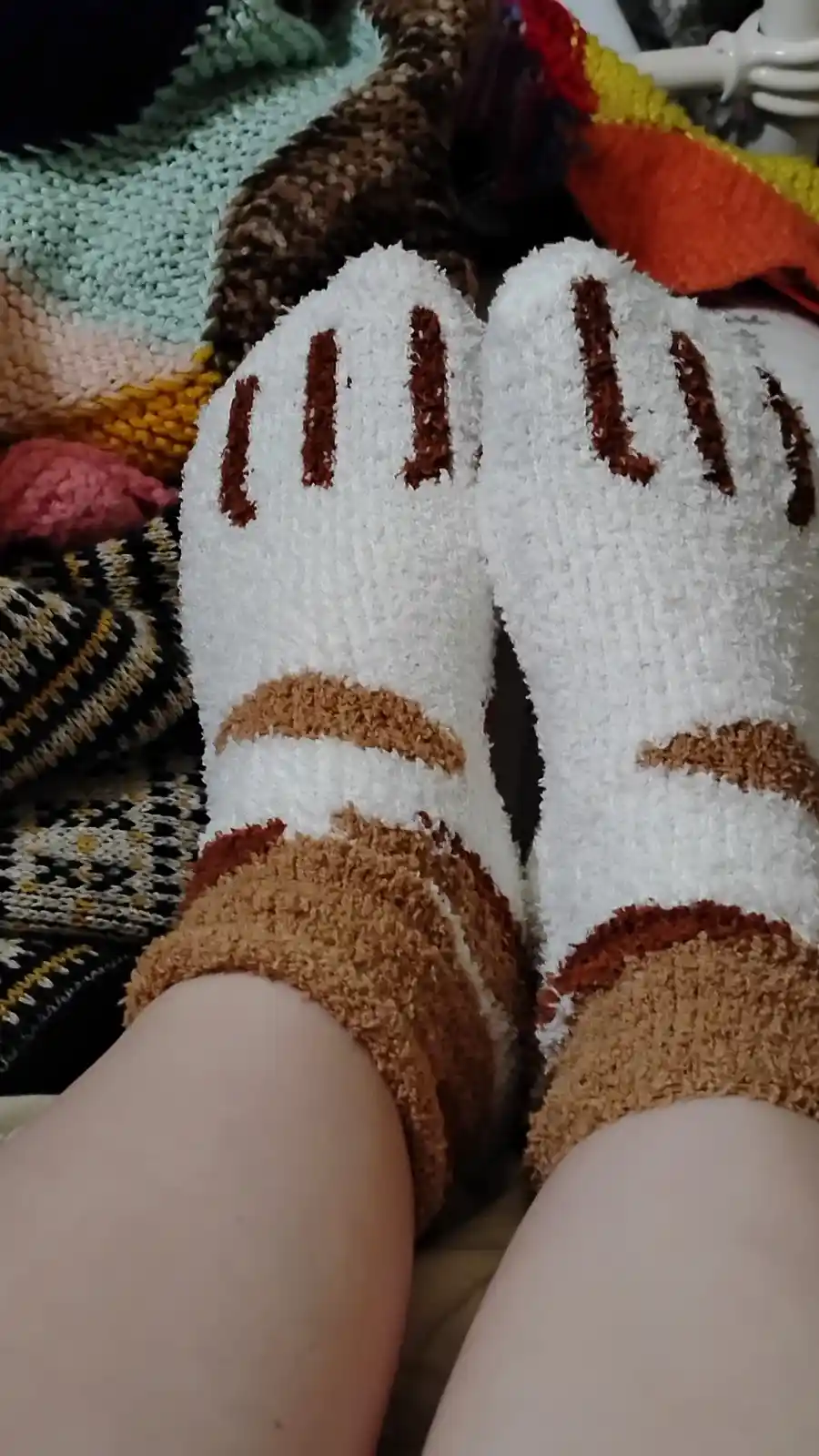 A close-up photo shows a person's feet wearing fluffy white and brown socks that resemble cartoon animal paws with brown…