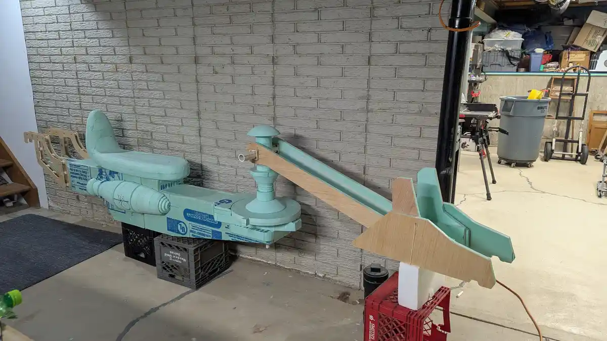 A homemade spaceship model, painted light teal, is constructed from insulation foam and wooden pieces, resting on plastic…