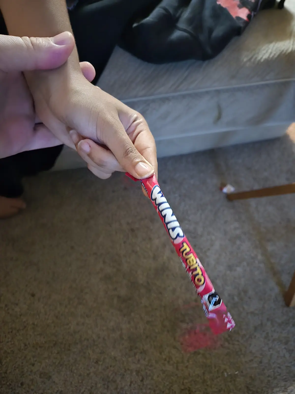 A person's hand holds a partially unwrapped red candy bar labeled 'MINIS TUBITO' with the wrapper torn at the end, set…