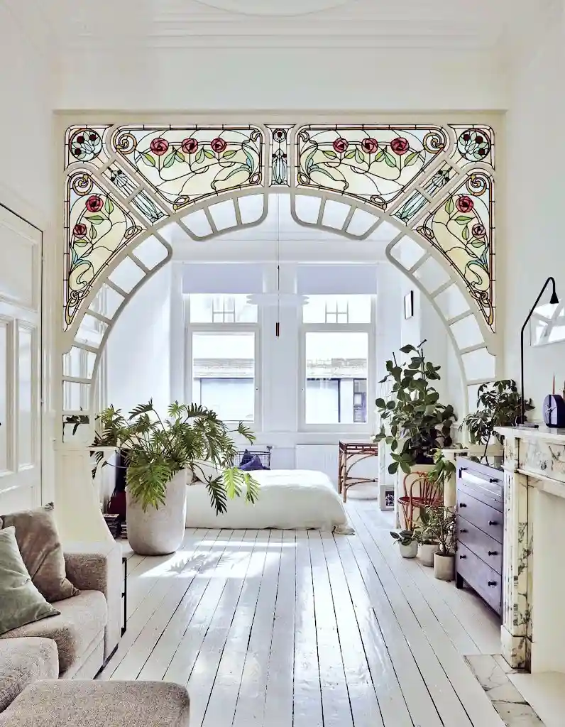 A bright, airy room with white wooden floors and ornate stained-glass archway featuring floral patterns. The space is filled…