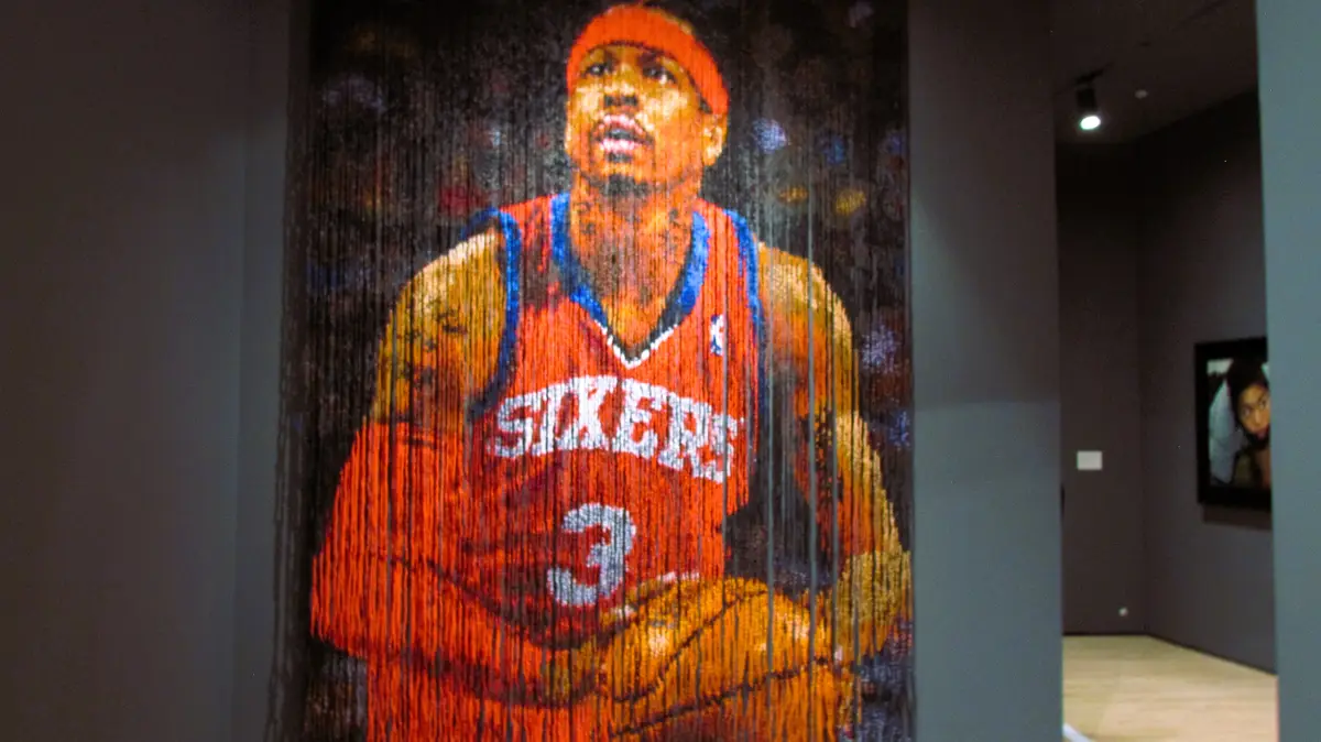 A beaded curtain art installation depicts a basketball player in a red 'Sixers' jersey with the number 3, rendered in…